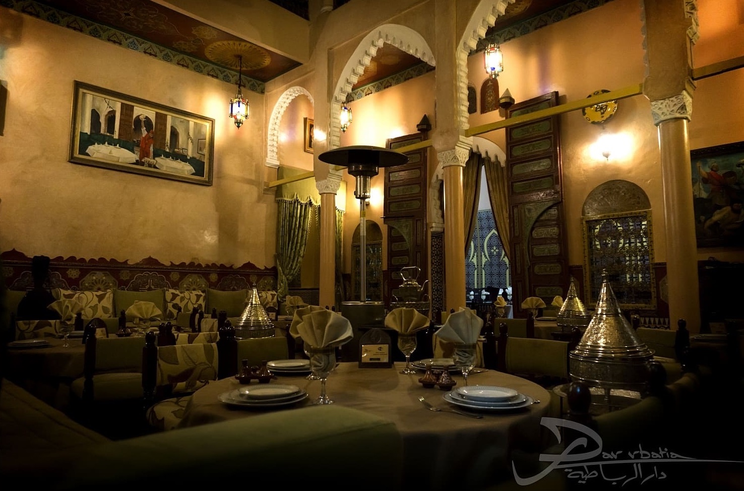 Salle principale de Dar Rbatia : arcades en plâtre ciselé, plafond peint, lanternes et tables dressées