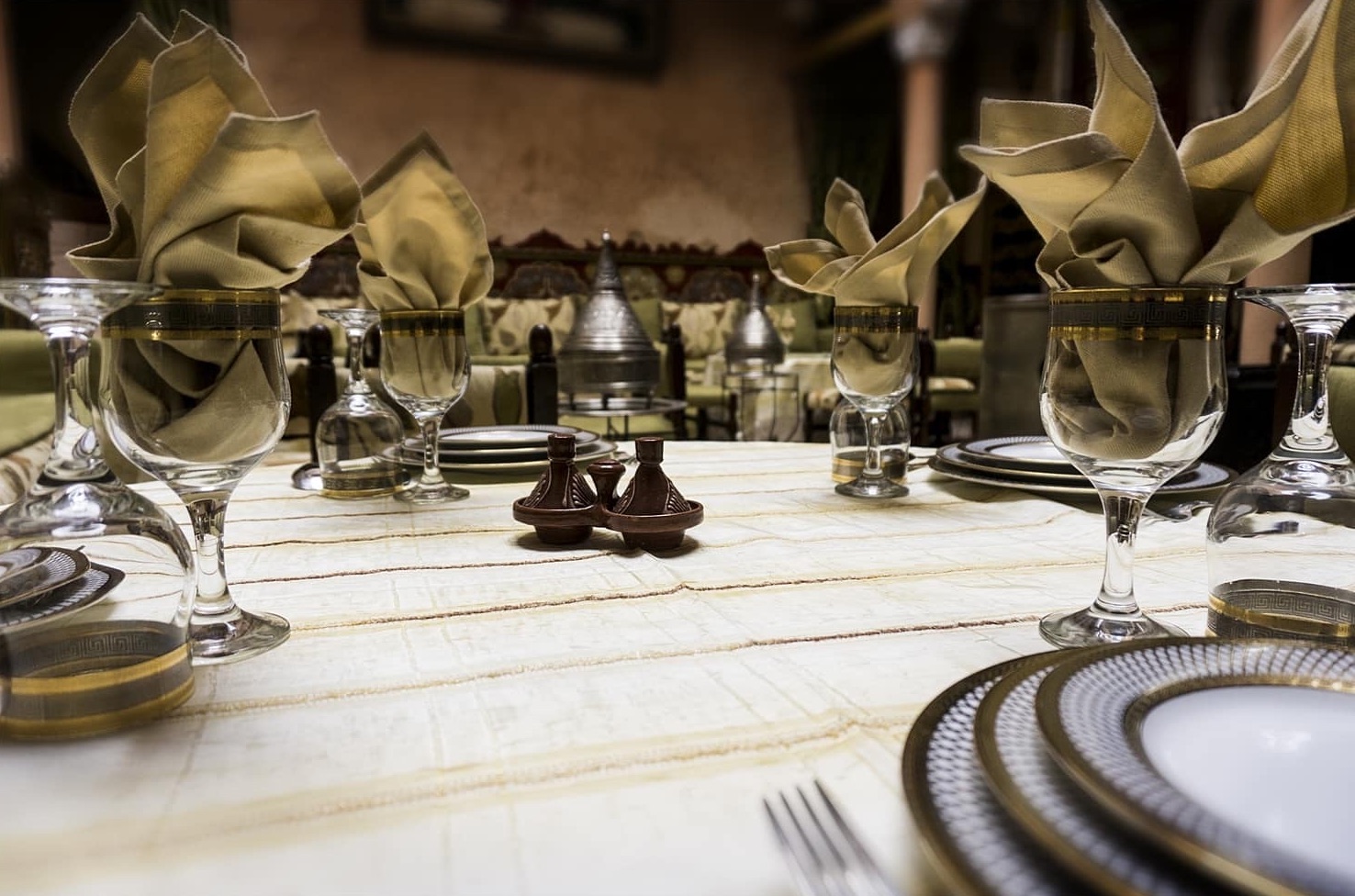 Table dressée : serviettes pliées dans des verres à filet doré, petits tajines à épices