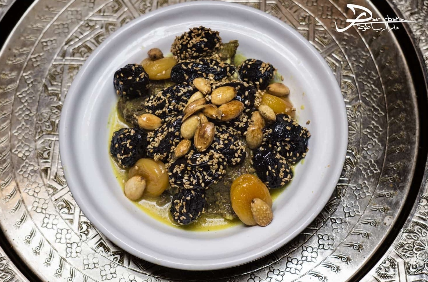 Tajine de bœuf aux pruneaux, abricots et amandes, parsemé de sésame, sur un plateau en argent ciselé